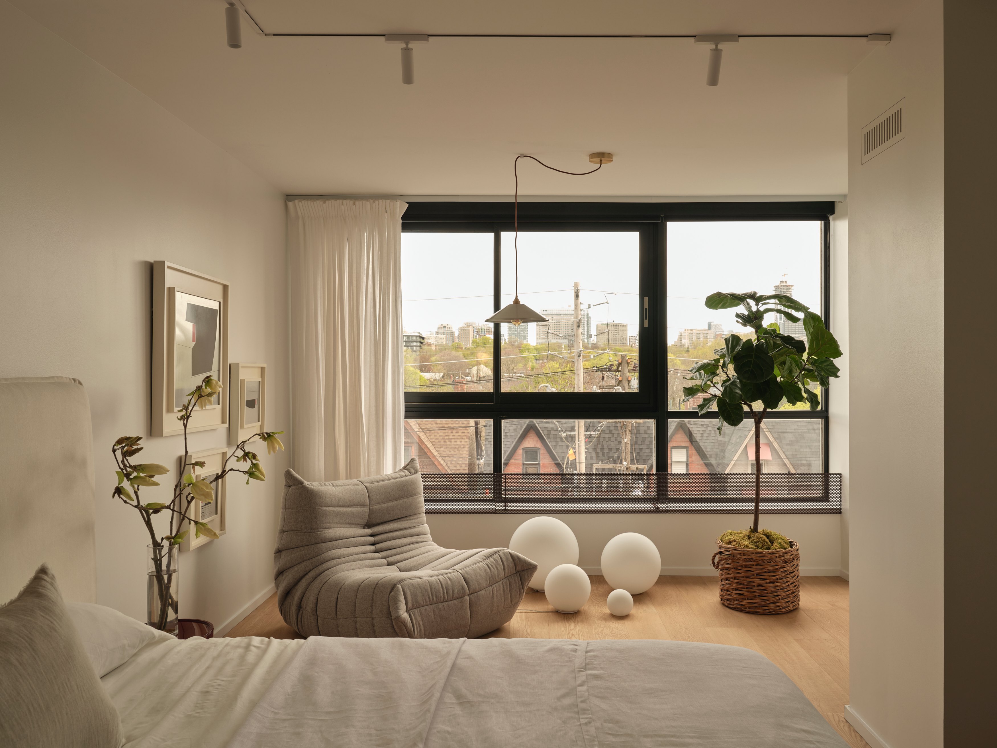 Bedroom with grey lounge chair and large window overlooking Toronto rooftops
