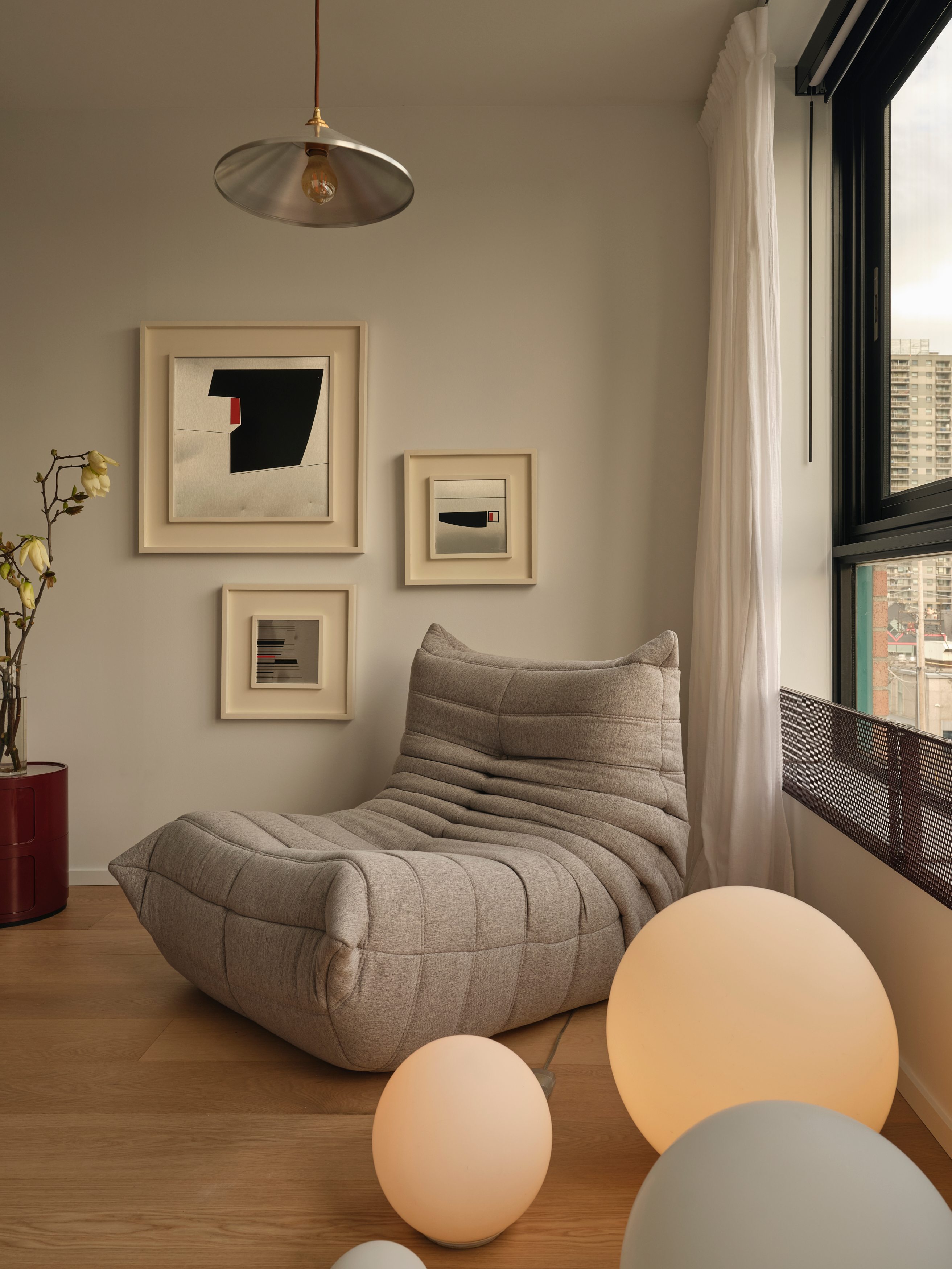 Reading corner with grey lounge chair, gallery wall, and city view