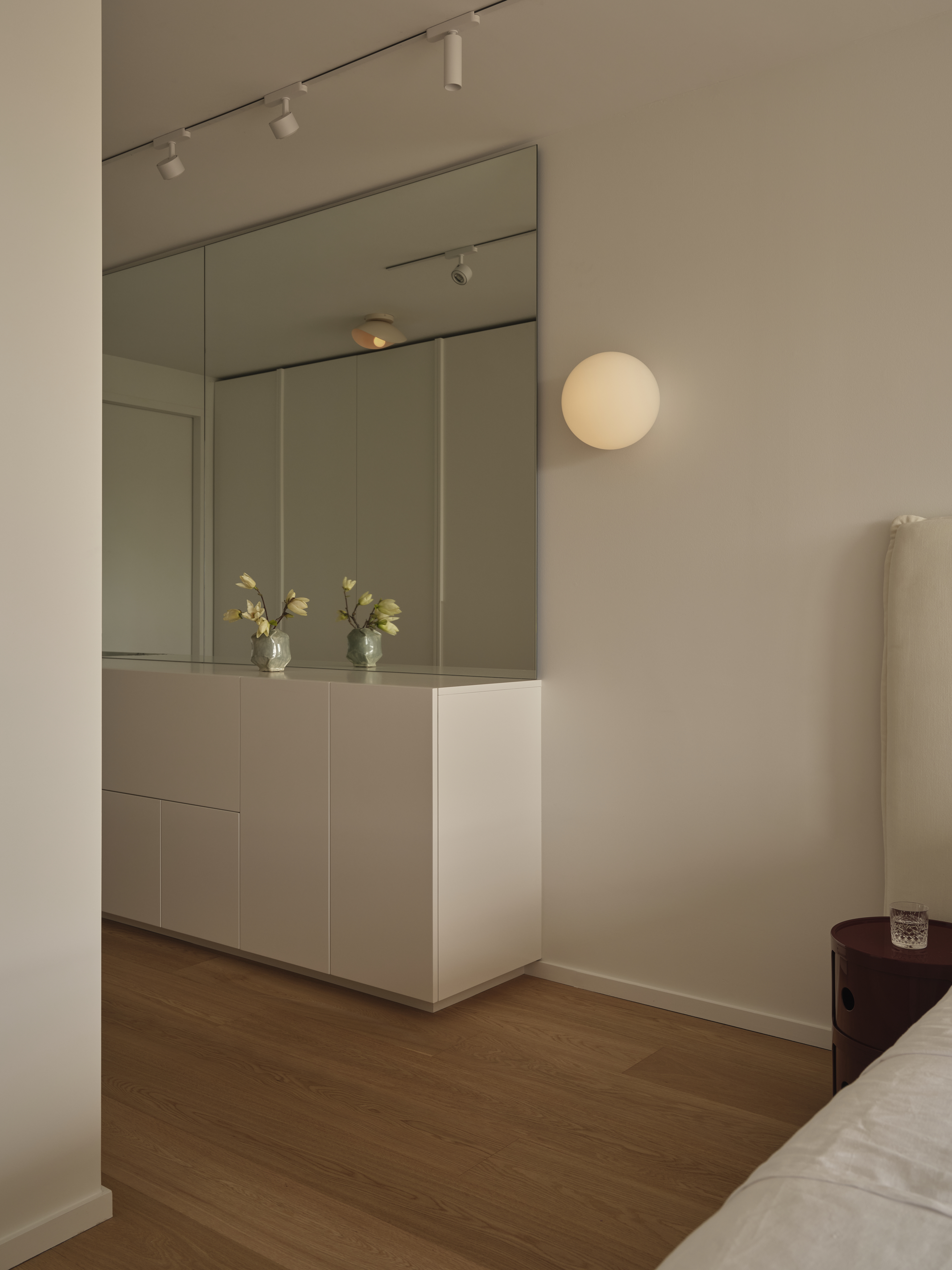 Bedroom with mirrored built-in cabinet, magnolia stems, and globe sconce