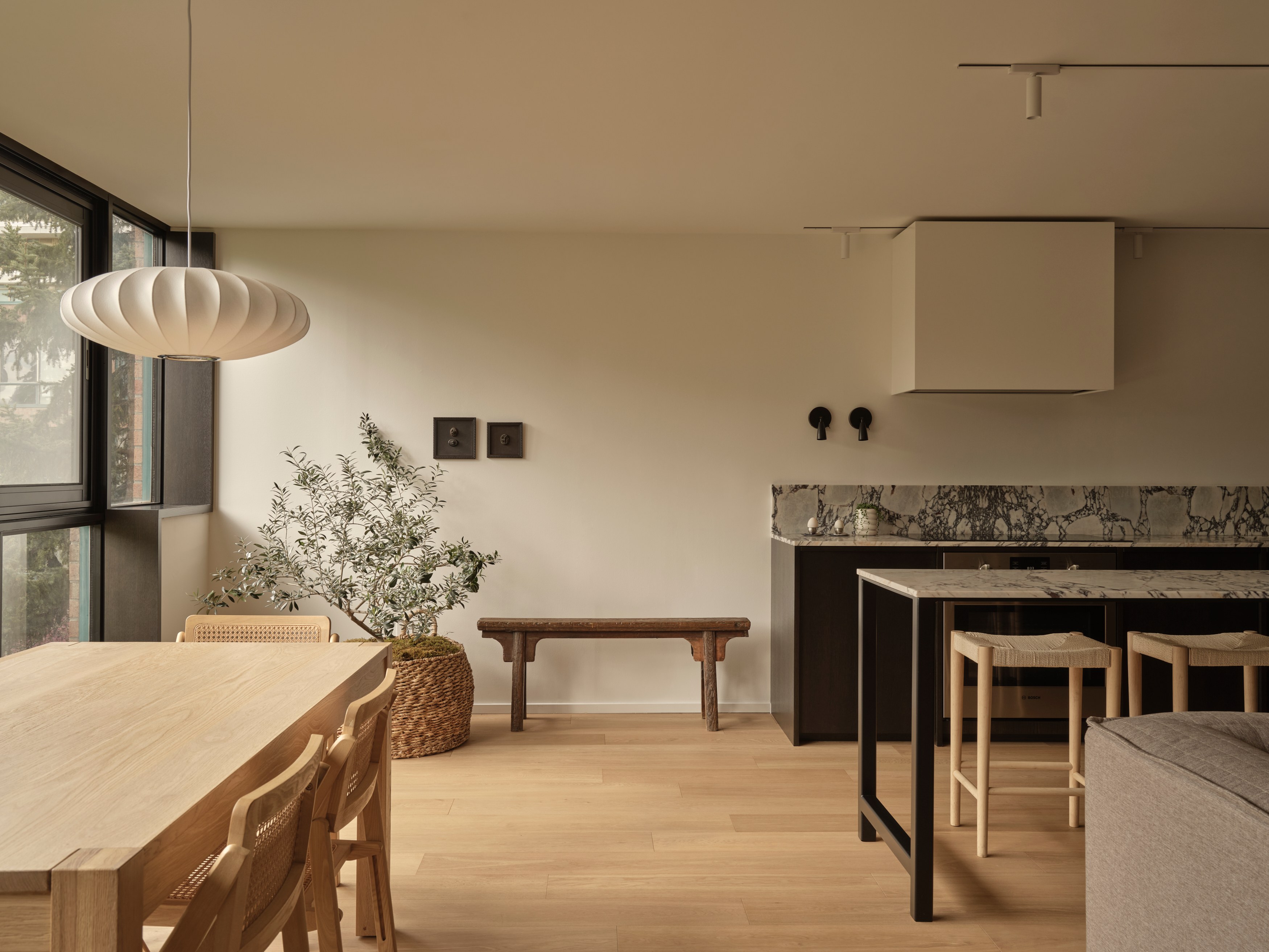 Open living and dining area with light oak table, cane chairs, and olive tree