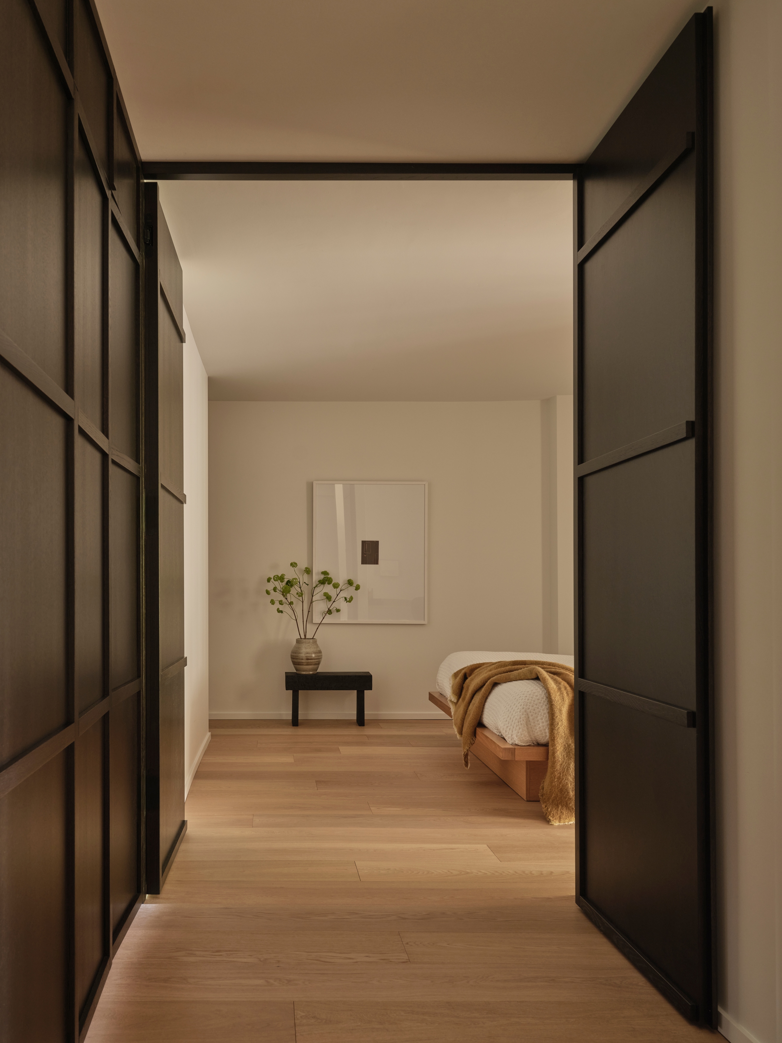 Hallway framed by black pivot doors and dark oak paneling leading to the bedroom