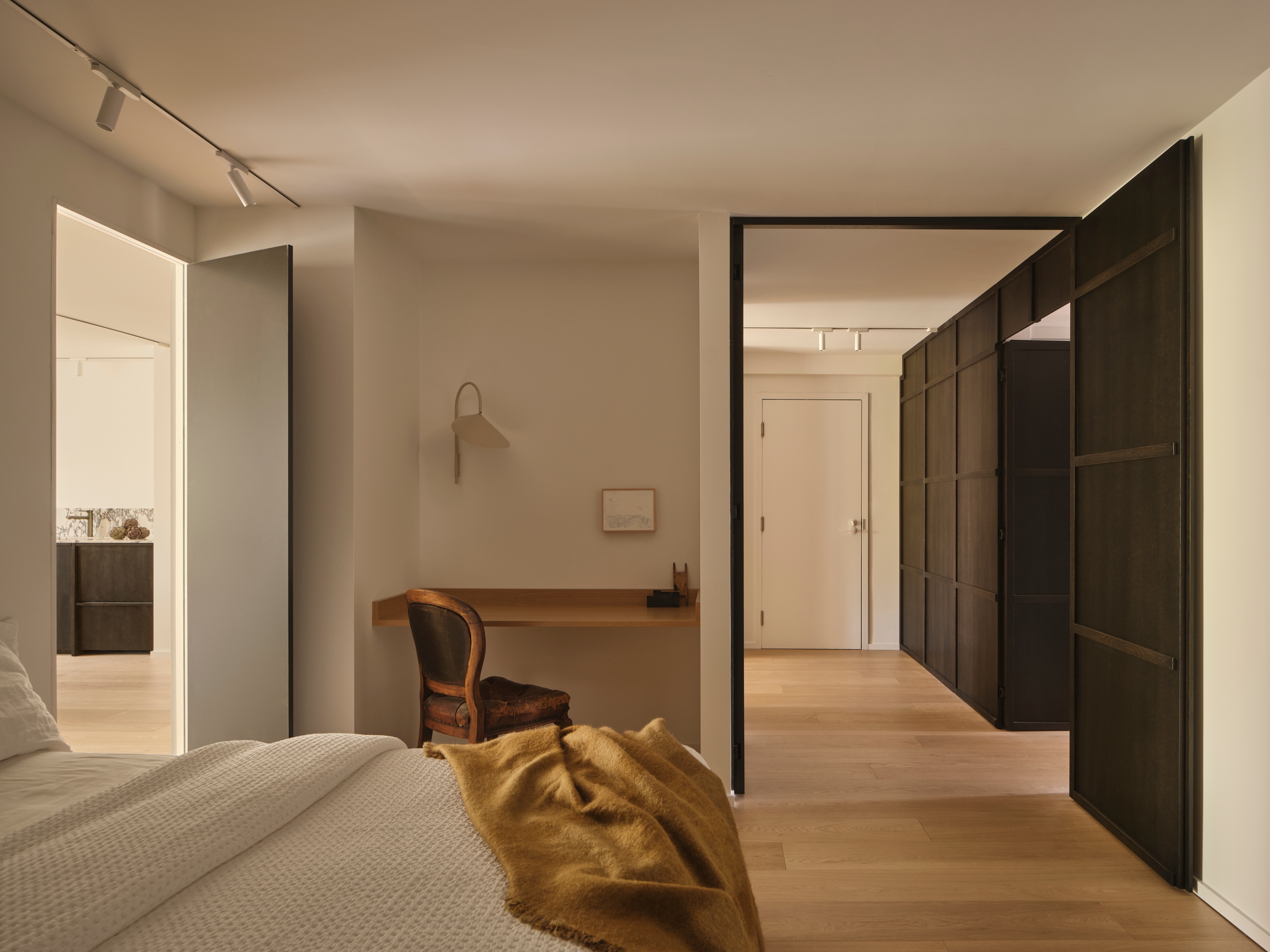 Bedroom looking through a black pivot door to a hallway lined with dark oak wardrobes