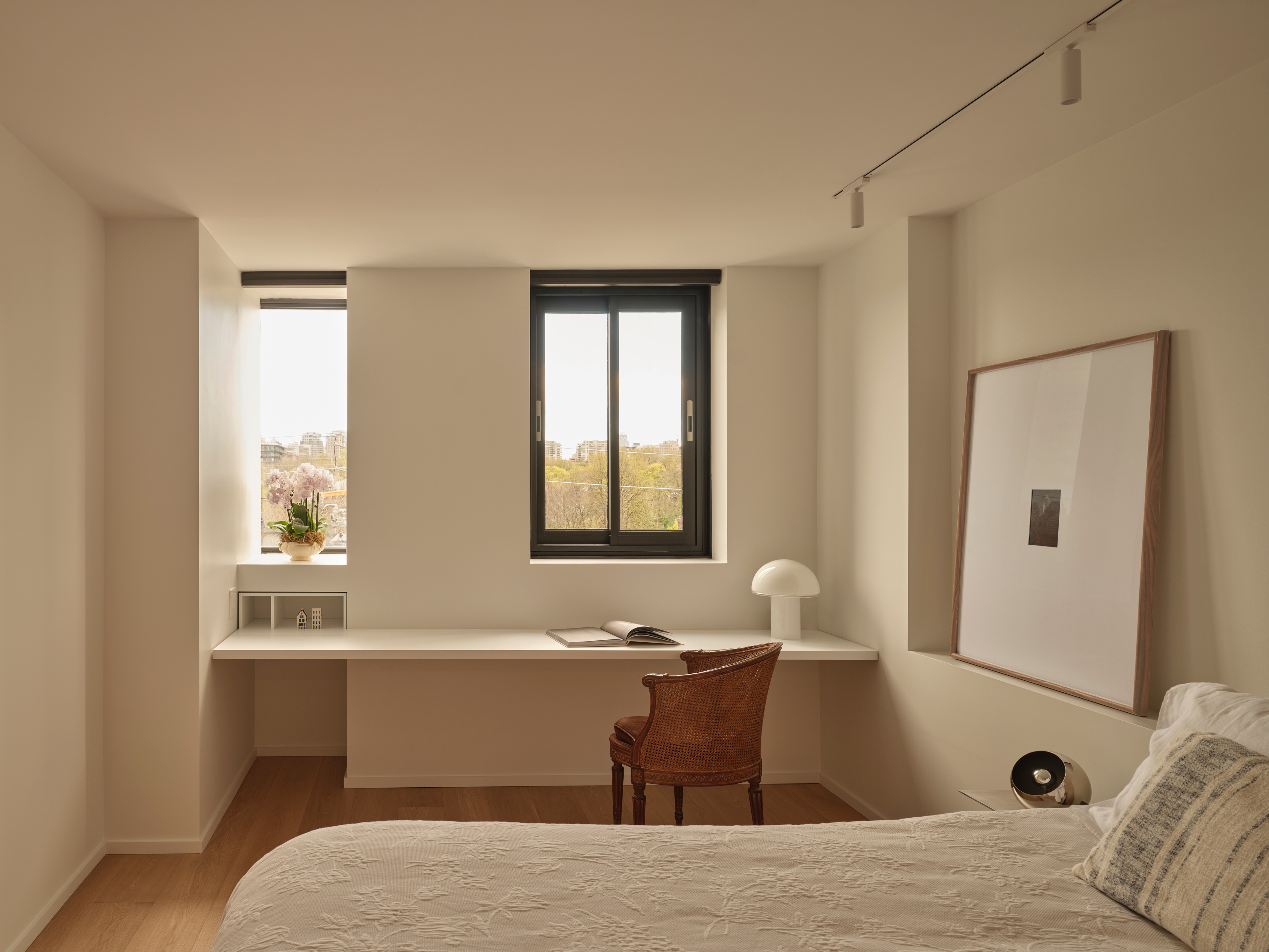 Bedroom with built-in white desk, vintage cane chair, and window over the park