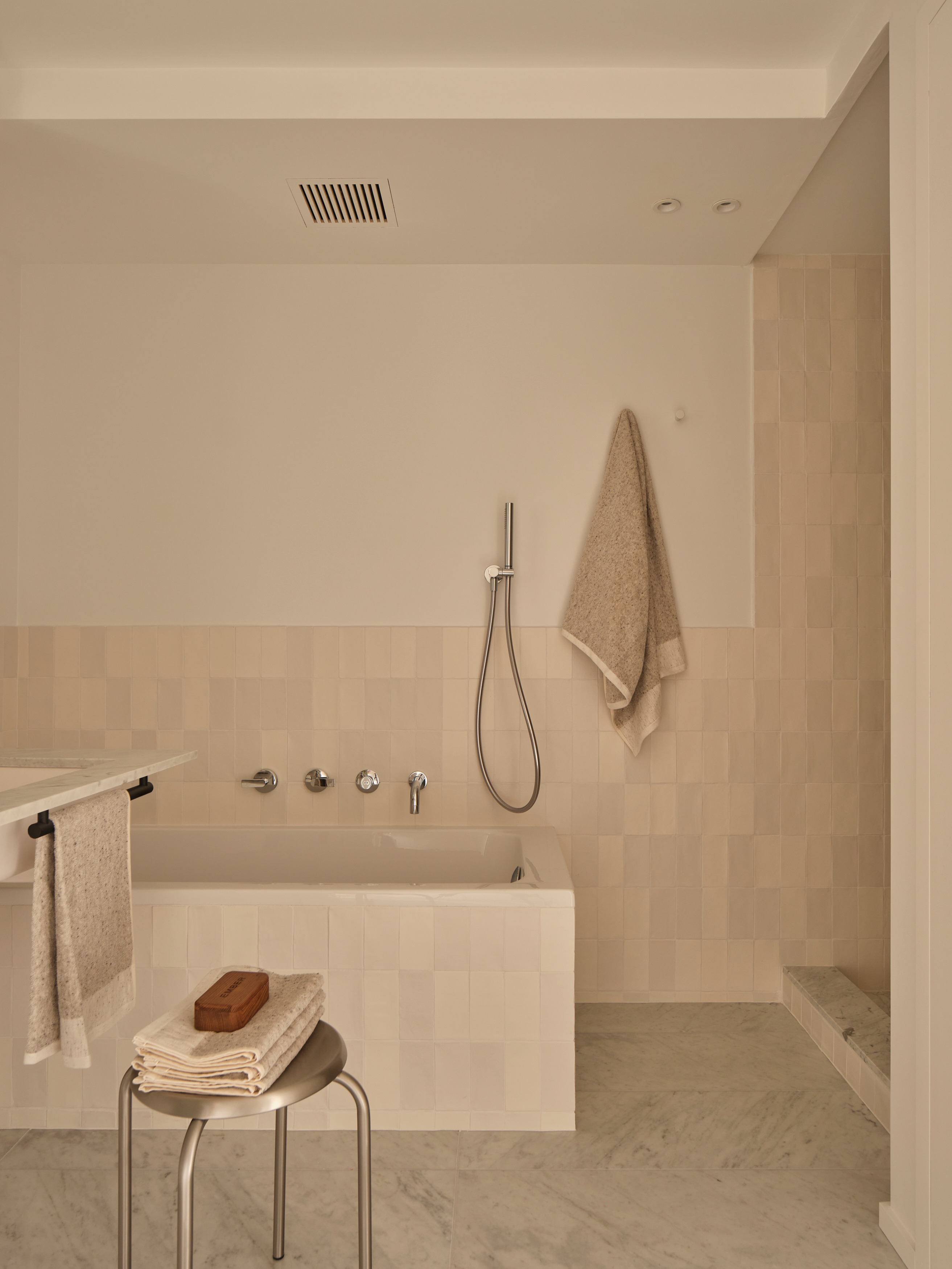 Bathroom with tiled bathtub, handheld shower, hanging towels, and marble floor