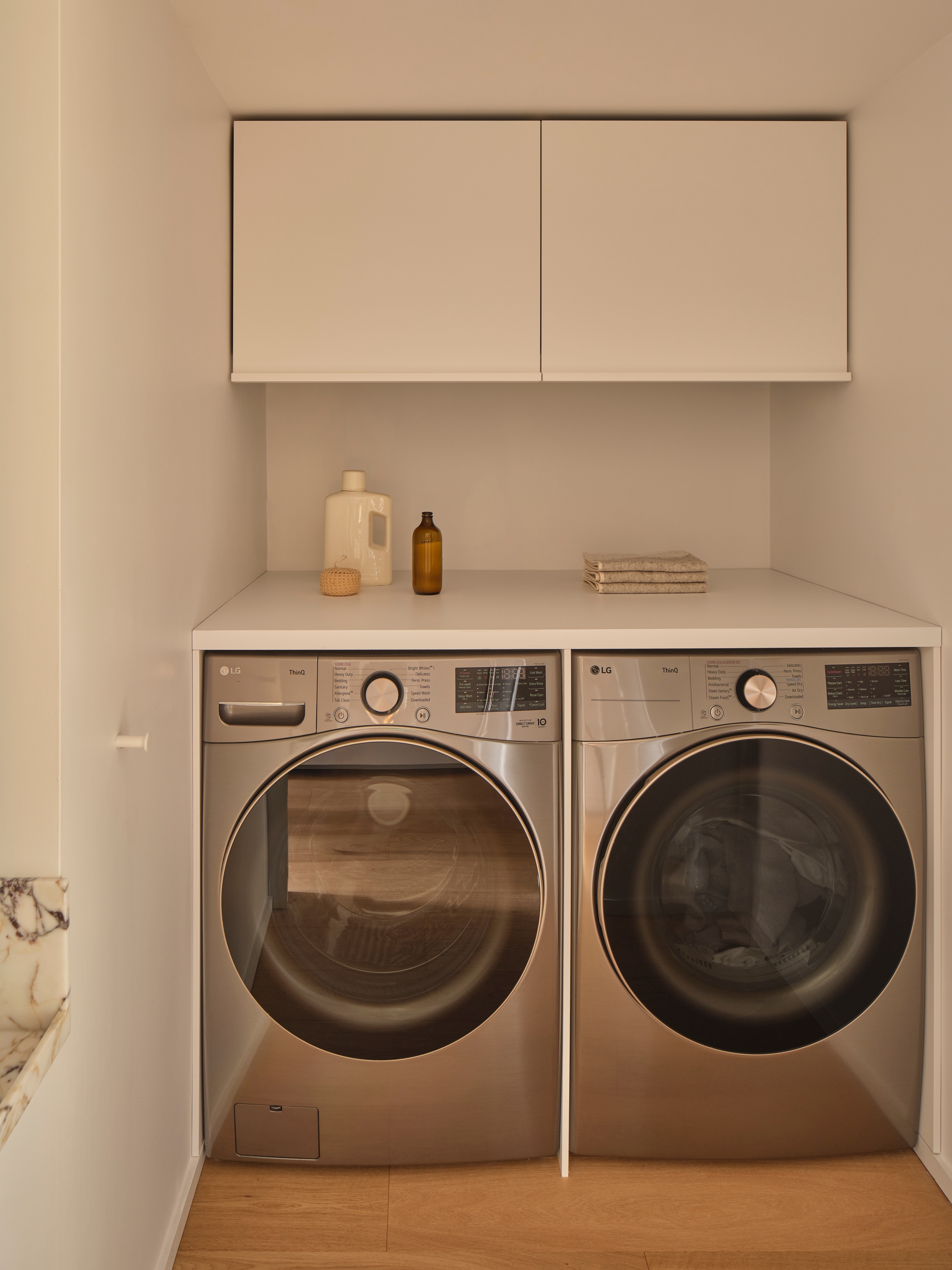 Renovated laundry room with front-load units, custom surround, and Viola marble sink