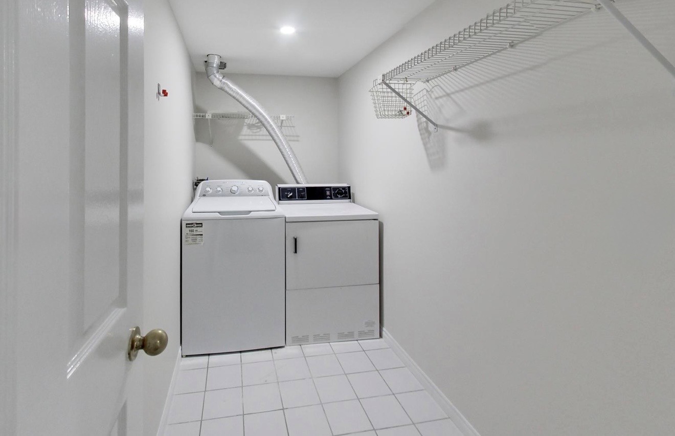 Original laundry room with exposed ducting, wire shelving, and top-load machines before renovation